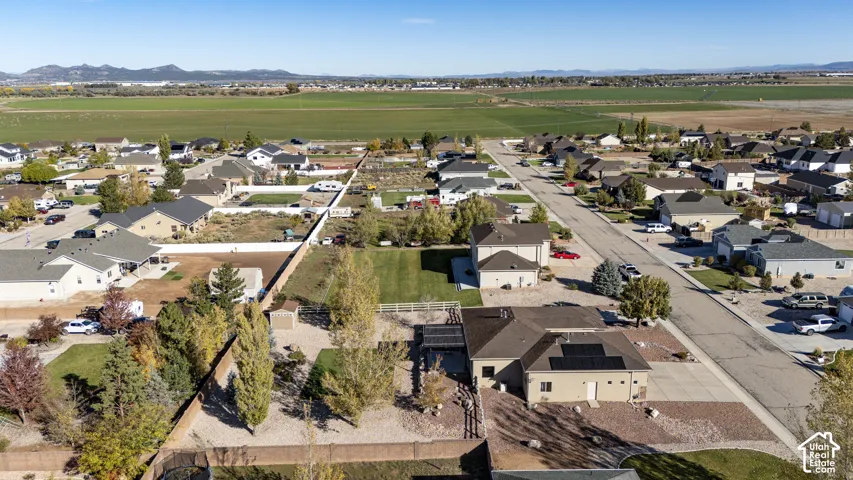Aerial perspective showcasing a property with roof-mounted solar panels, a covered patio structure, and a fenced rear yard with mature trees