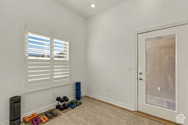 High-ceiling interior space featuring white plantation shutters, neutral-tone carpeting, and an exterior door with a glass insert