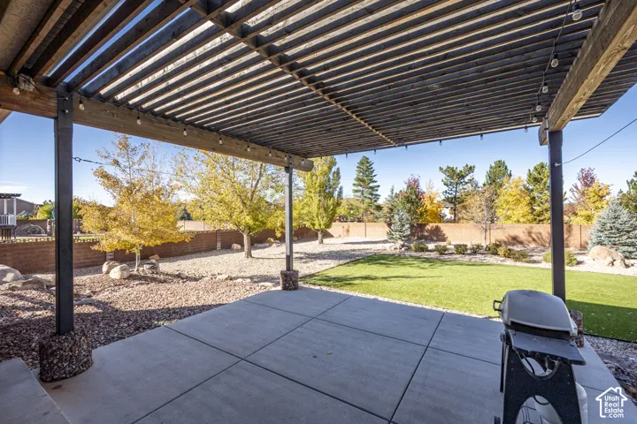 Outdoor living space featuring a concrete patio, wood-slat pergola, artificial turf, gravel landscaping, and a masonry perimeter wall