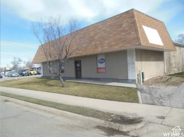 Commercial exterior featuring a mansard roofline, vertical panel siding, concrete sidewalk, and paved frontage