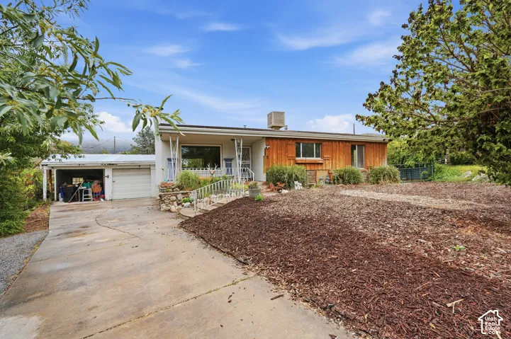 Single-story residence featuring wood-paneled siding, attached two-car garage, concrete driveway, and stone-retained landscaping