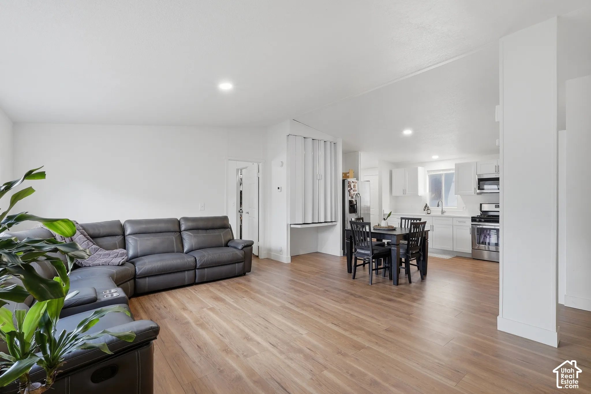 Open-concept interior featuring wood-finish flooring, recessed lighting, and kitchen cabinetry with integrated stainless steel appliances