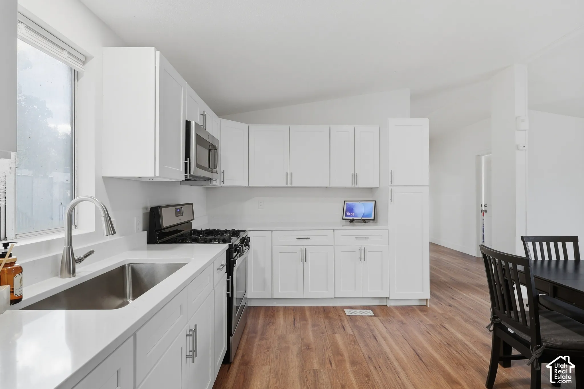 Kitchen featuring white shaker-style cabinetry, quartz countertops, stainless steel undermount sink with a gooseneck faucet, and wood-finish flooring