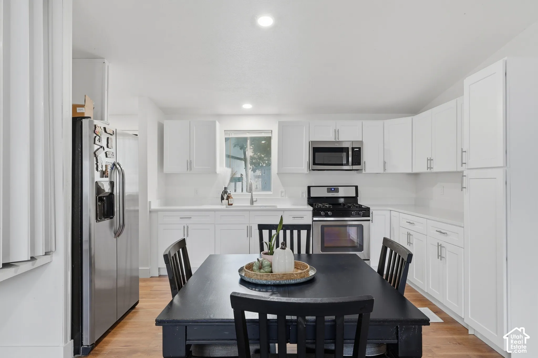 Kitchen featuring white Shaker-style cabinetry, stainless steel appliances, wood-finish flooring, recessed lighting, and a window above the sink
