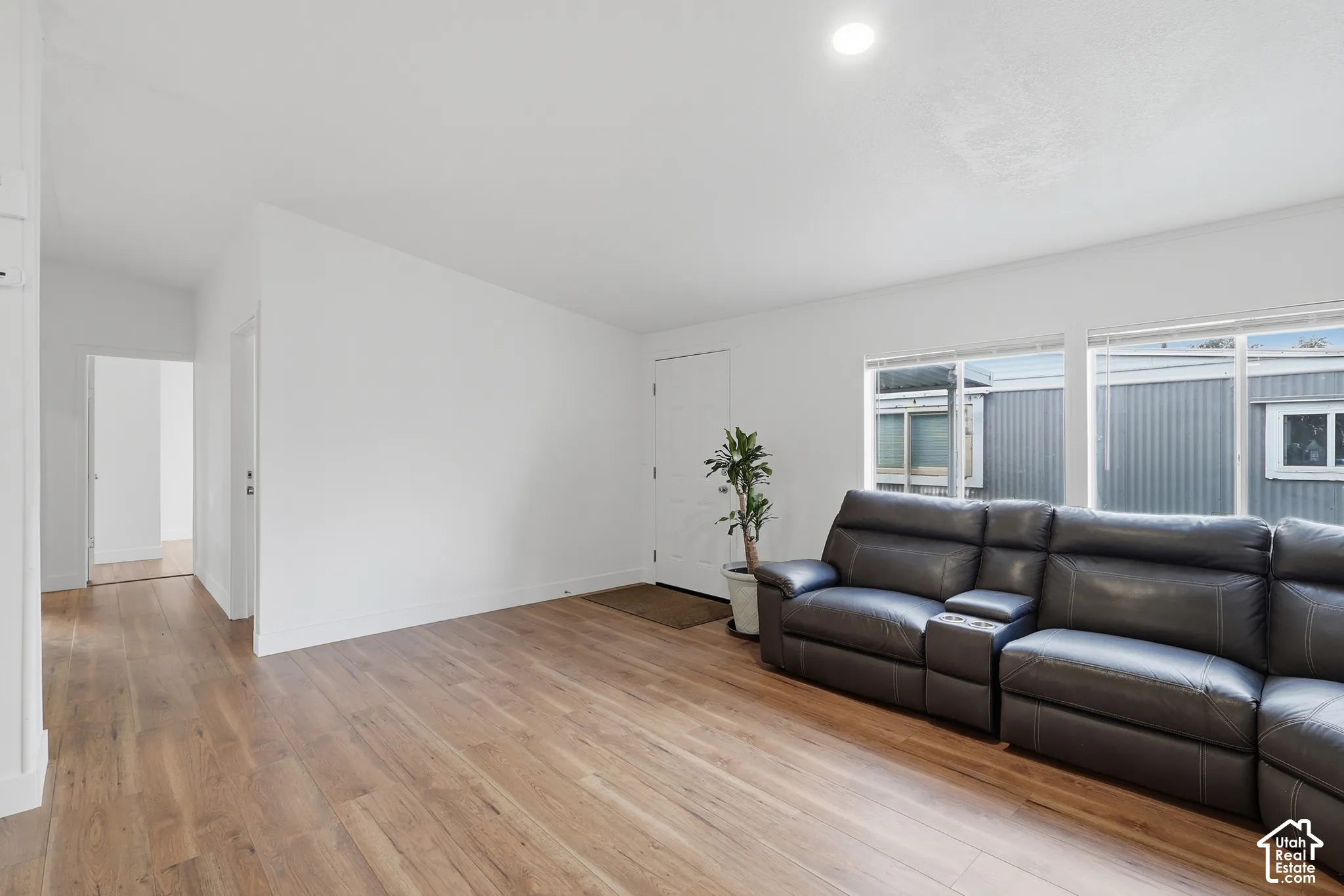 Interior space featuring wood-finish flooring, white walls, recessed ceiling lighting, and large dual-pane windows with horizontal blinds