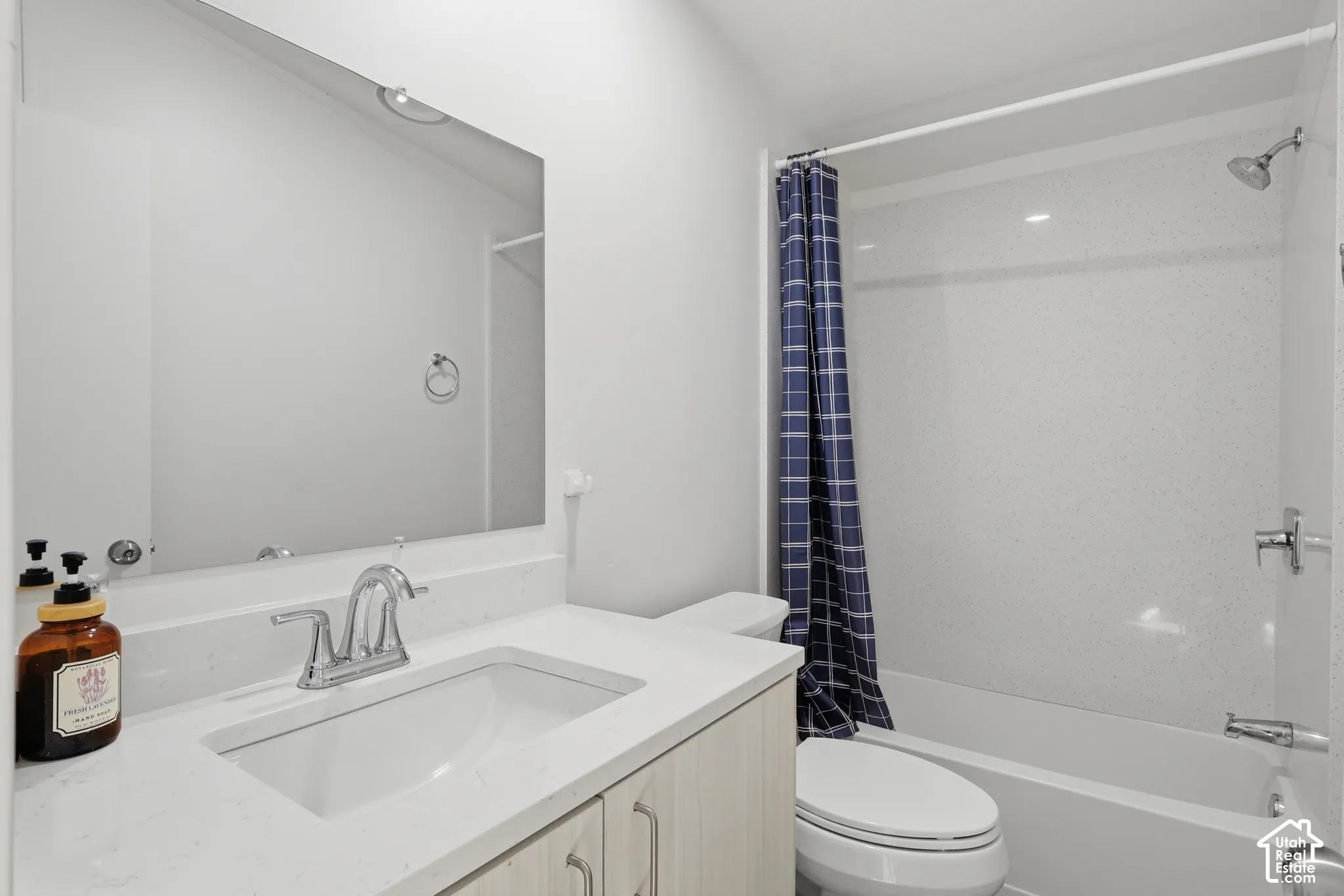 Full-width vanity mirror, quartz countertop with an integrated basin, wood-finish cabinetry, and a tub-shower combination with a surround enclosure