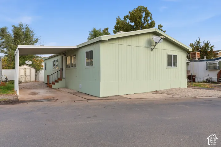 Single-level exterior with vertical siding, attached carport, and standalone storage shed