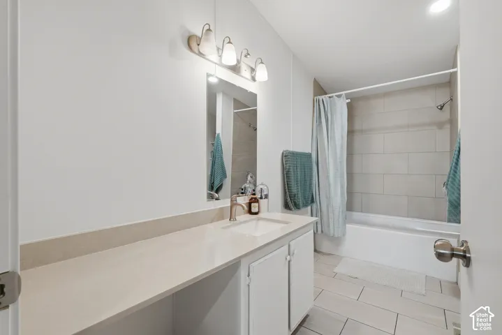 Bathroom featuring a vanity with a solid-surface countertop, rectangular undermount sink, multi-light fixture, mirror, and a tub-shower combination with large-format wall tiling and tile flooring