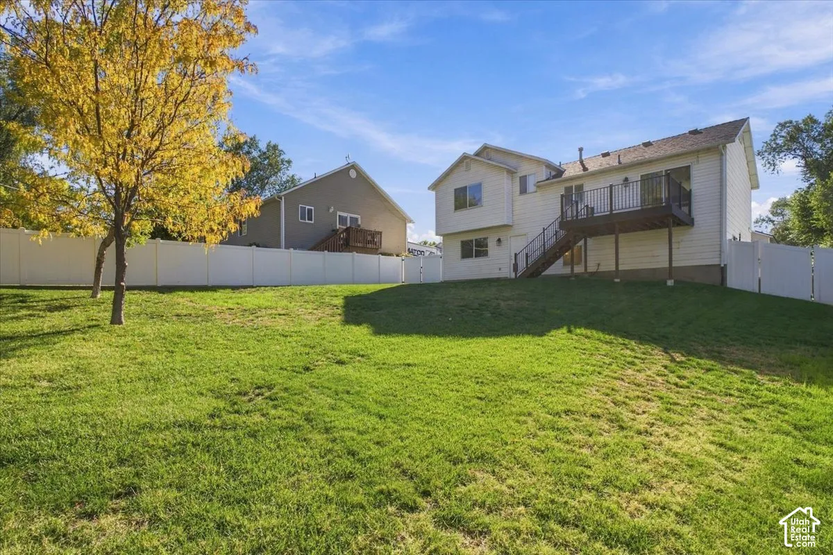 Expansive backyard featuring a manicured lawn, full-perimeter white vinyl fencing, and an elevated deck with metal railings