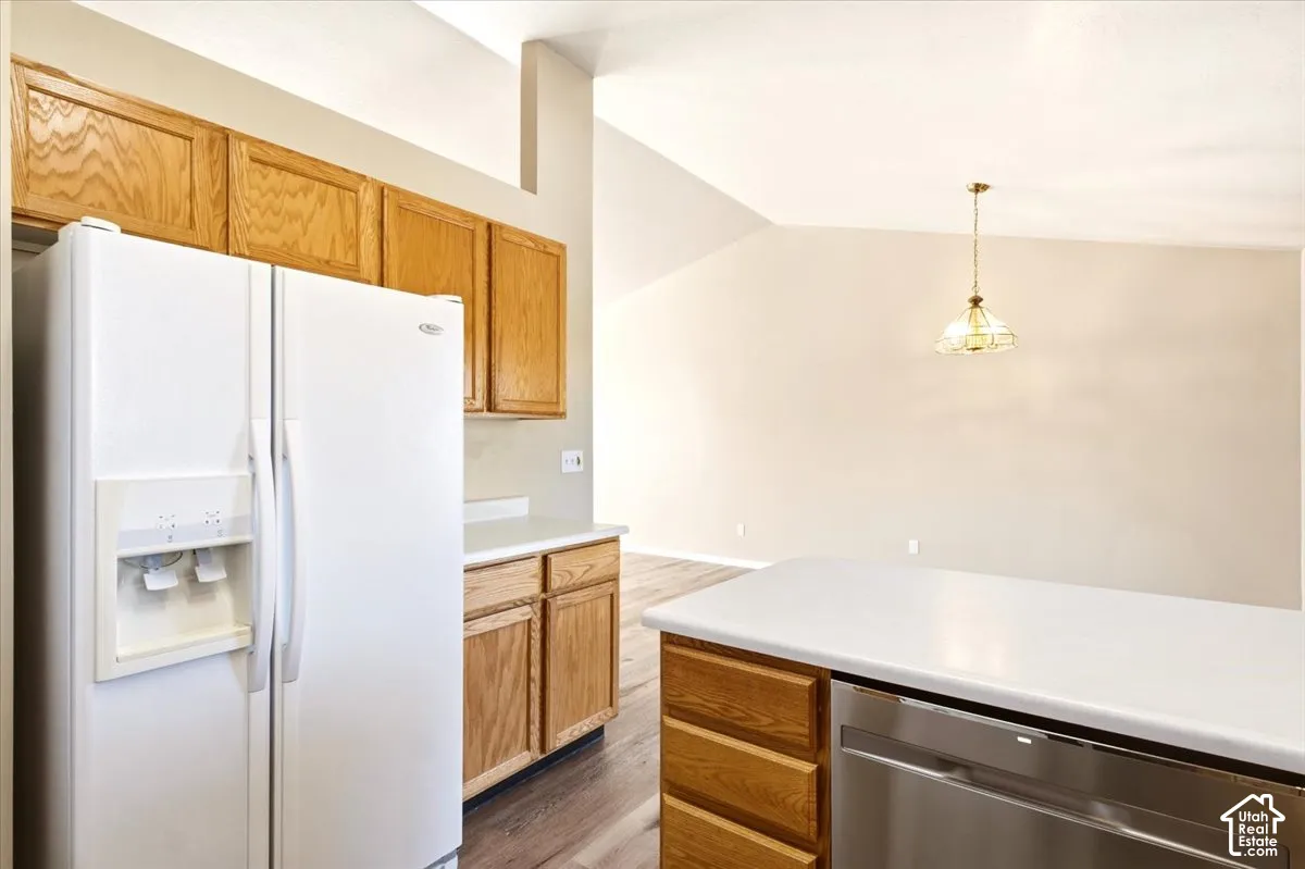 Kitchen featuring cabinetry with a natural wood finish, solid-surface countertops, wood-finish flooring, vaulted ceilings, and a suspended pendant light fixture