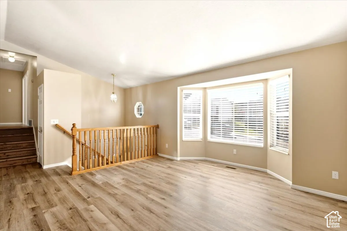 Vaulted ceilings, wood-finish flooring, bay window with integrated blinds, and wooden staircase railing