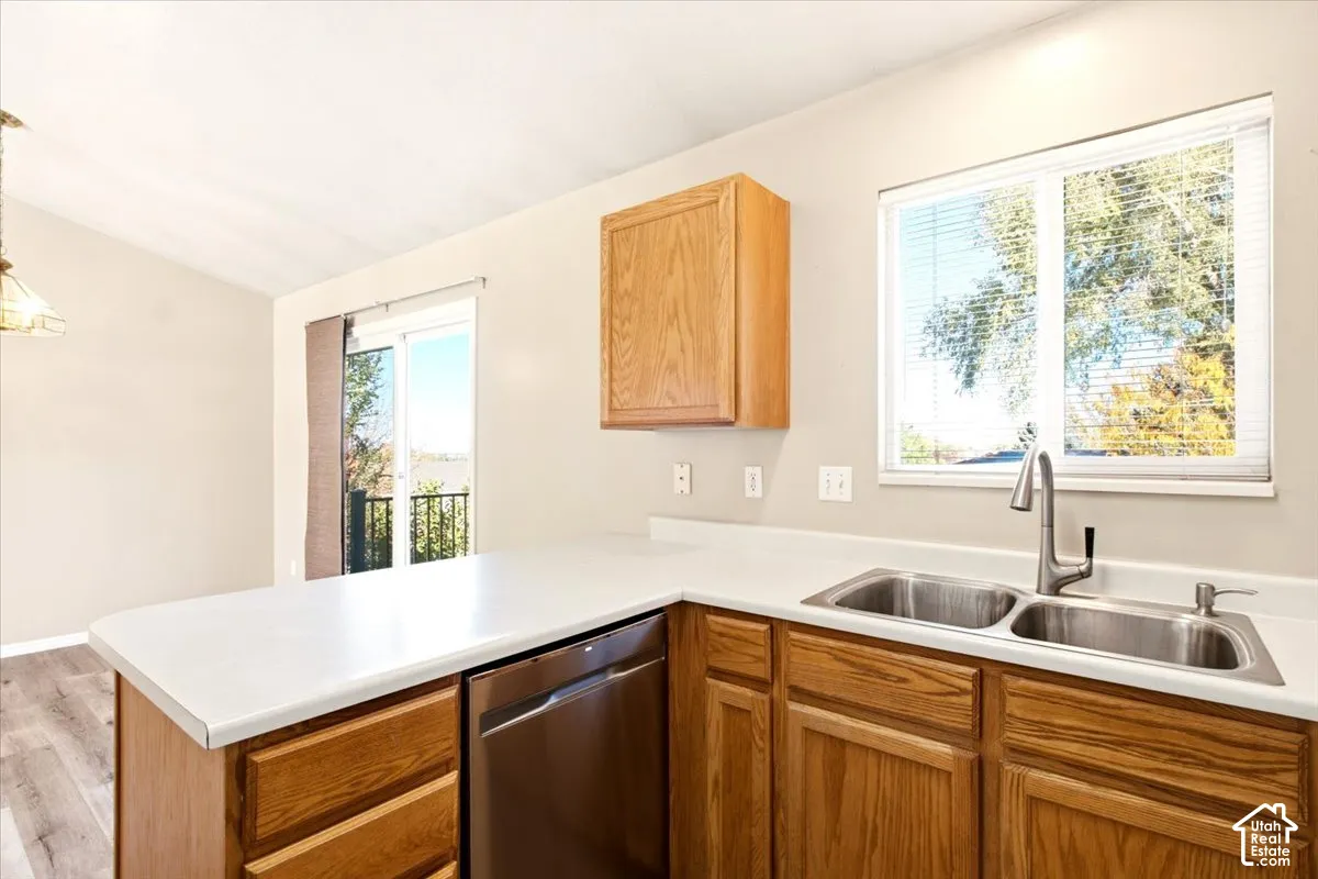 Kitchen featuring wood cabinetry, white solid-surface countertops, dual-basin stainless steel sink with a high-arch faucet, stainless steel dishwasher, and sliding glass door