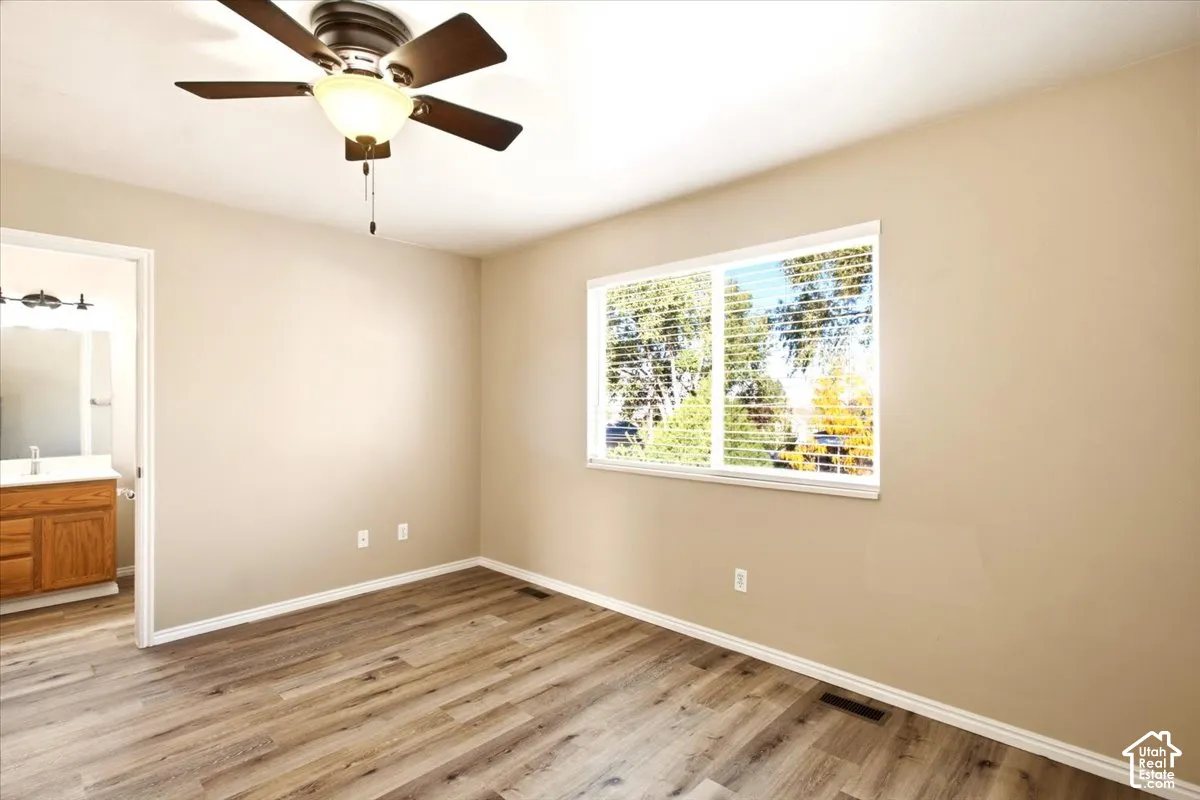 Room featuring wood-finish flooring, a ceiling fan with integrated lighting, a sliding window, and a door opening to a vanity area with a wooden cabinet