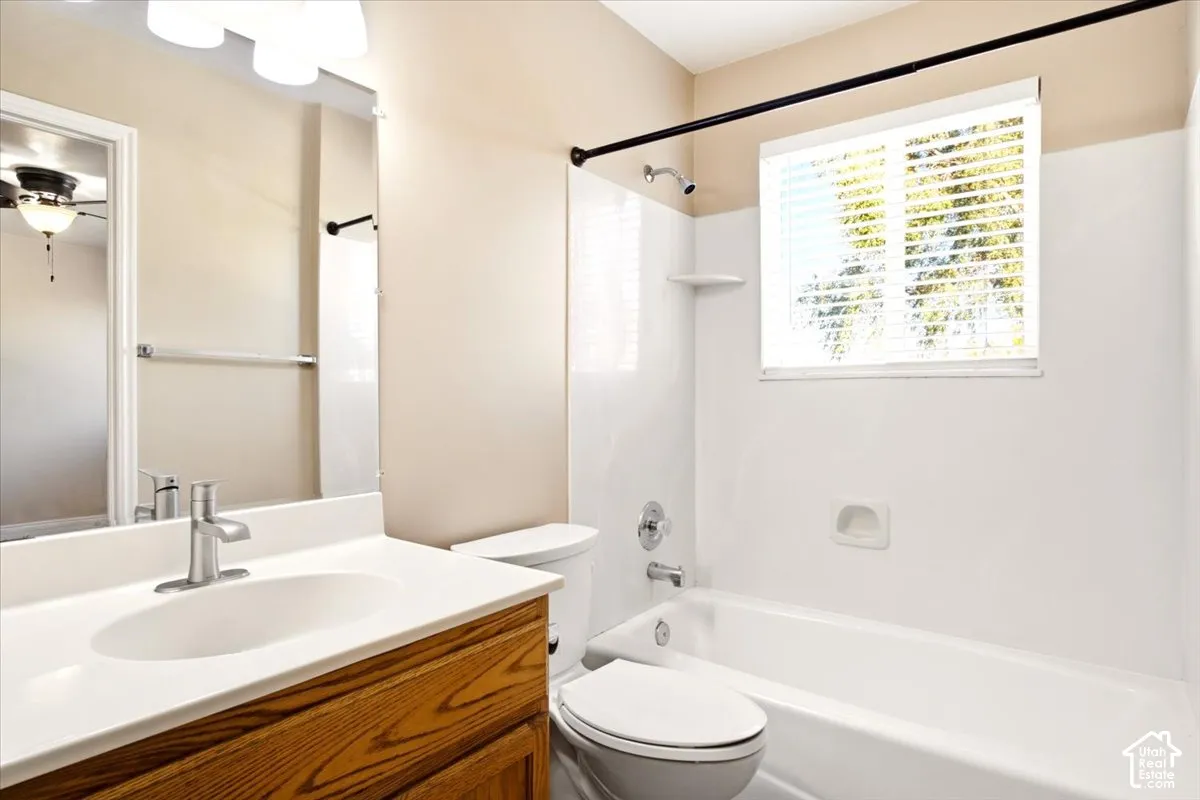 Bathroom featuring a wood-finish vanity with a white countertop, oval under-mount sink, chrome faucet, and a combination tub and shower with white surround