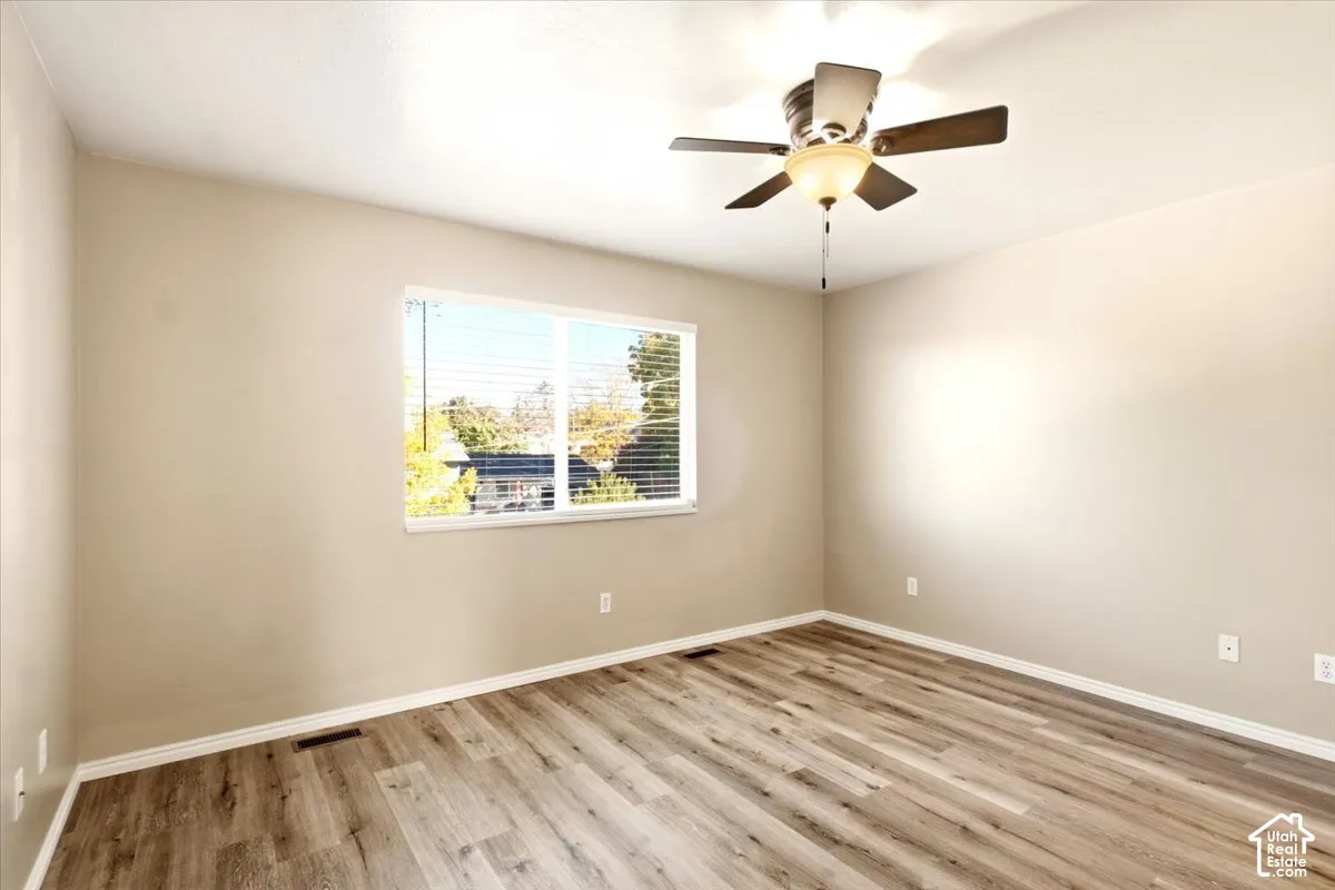Neutral-toned interior space featuring wood-finish flooring, a large single-pane window with horizontal blinds, and a ceiling fan with integrated lighting