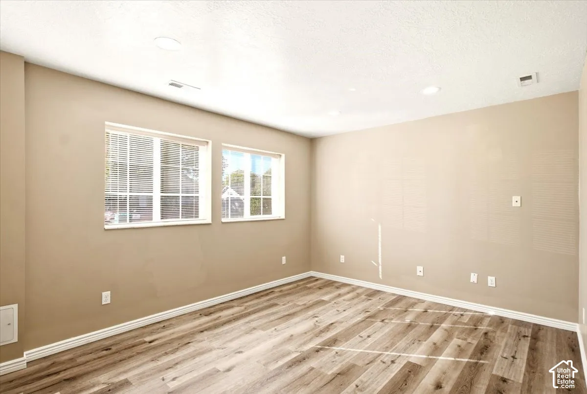 Room featuring neutral-toned walls, wood-finish flooring, recessed lighting, and dual windows with integrated blinds