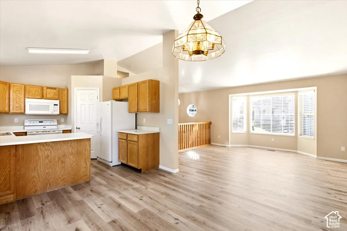 Kitchen featuring wood cabinetry, white appliances, and a peninsula counter, complemented by wood-finish flooring and a multi-pane pendant light fixture