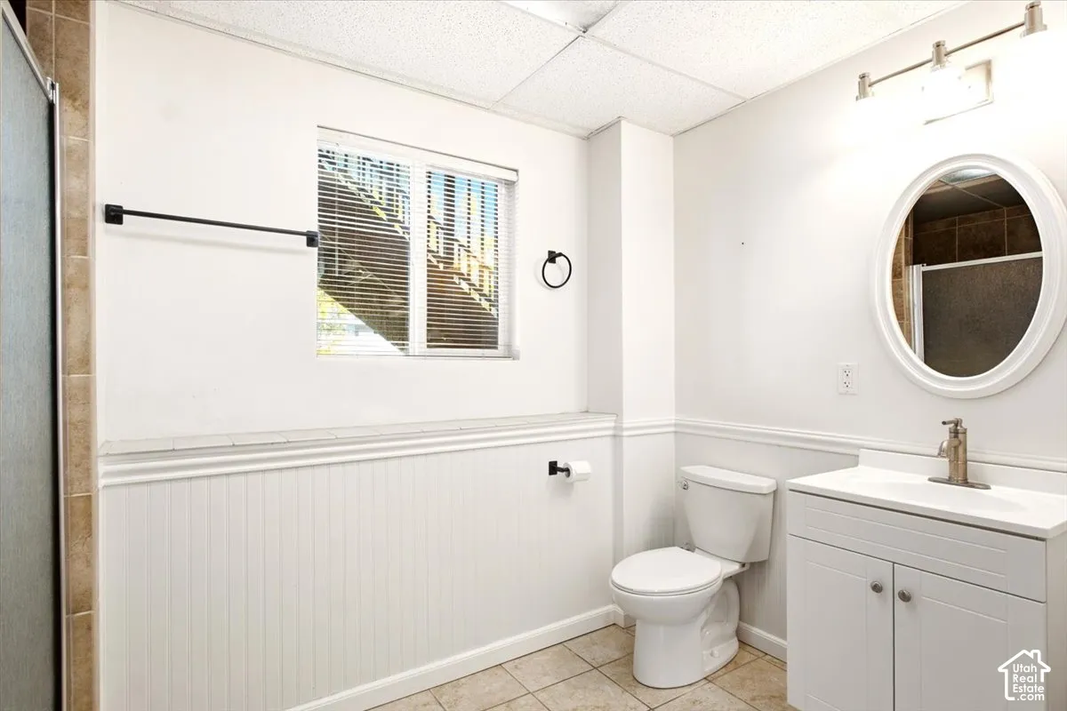 Bathroom featuring white beadboard wainscoting, a vanity cabinet with integrated sink, an oval mirror, matte black fixtures, and tile flooring