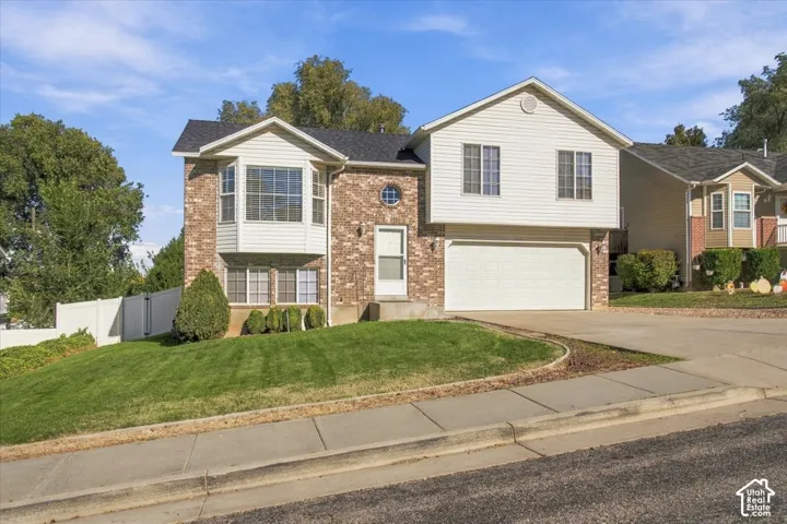 Multi-level exterior featuring a brick and horizontal siding facade, an attached two-car garage, bay window detailing, and a white privacy fence