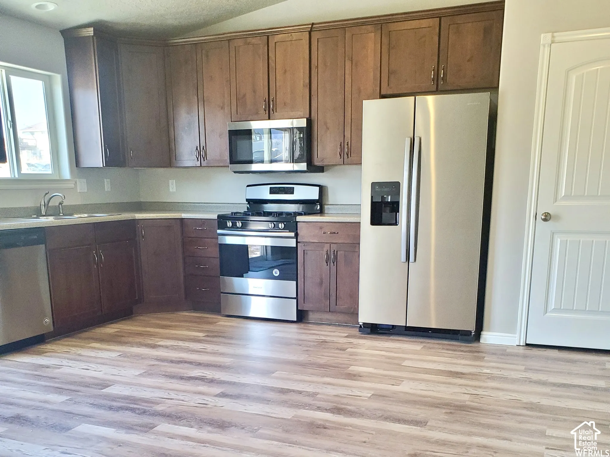 Kitchen featuring medium-tone wood cabinetry, stainless steel appliances, solid-surface countertops, and wood-finish flooring