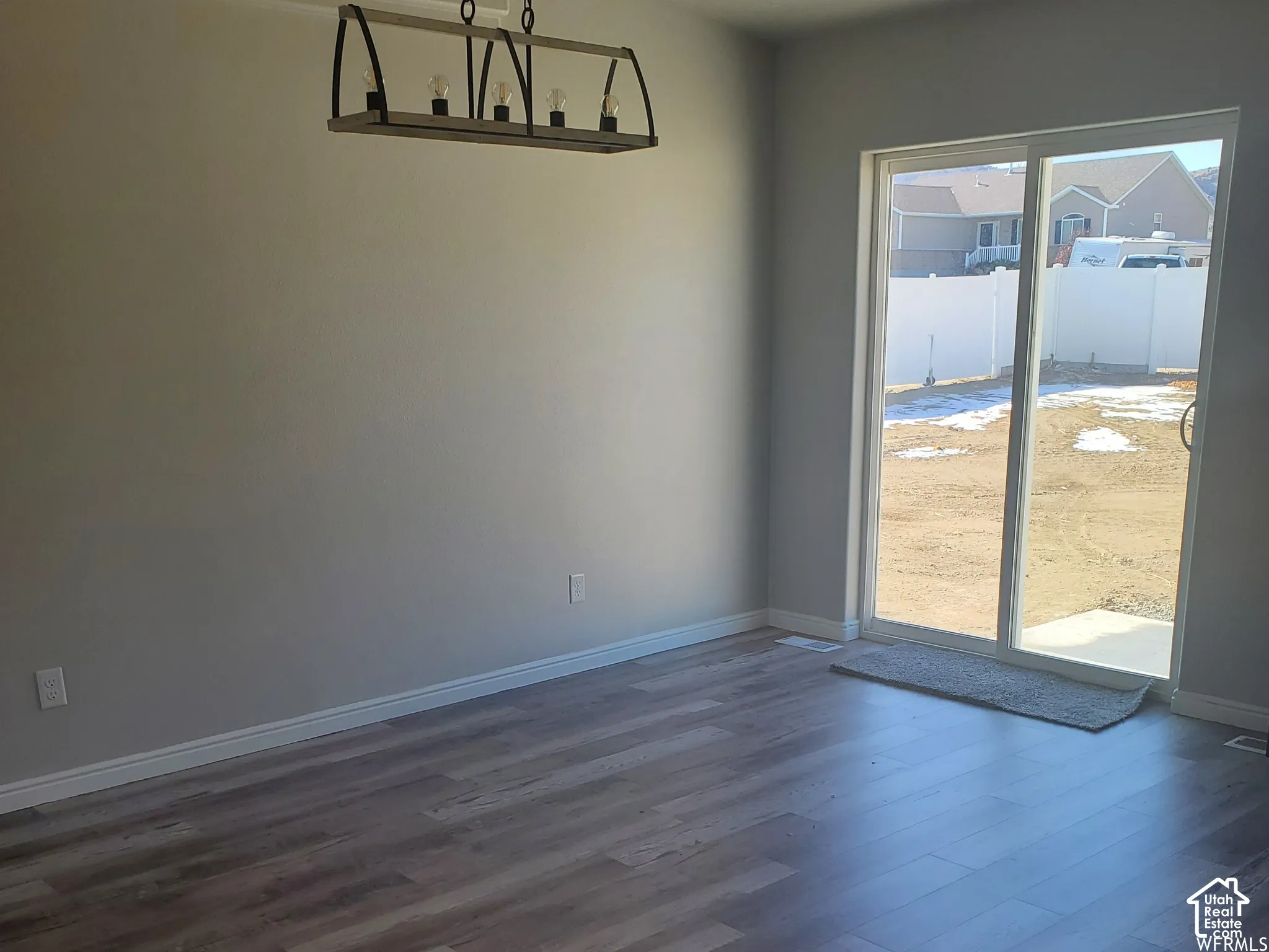 Wood-finish flooring, industrial-style multi-bulb chandelier, and large sliding glass door with access to the exterior
