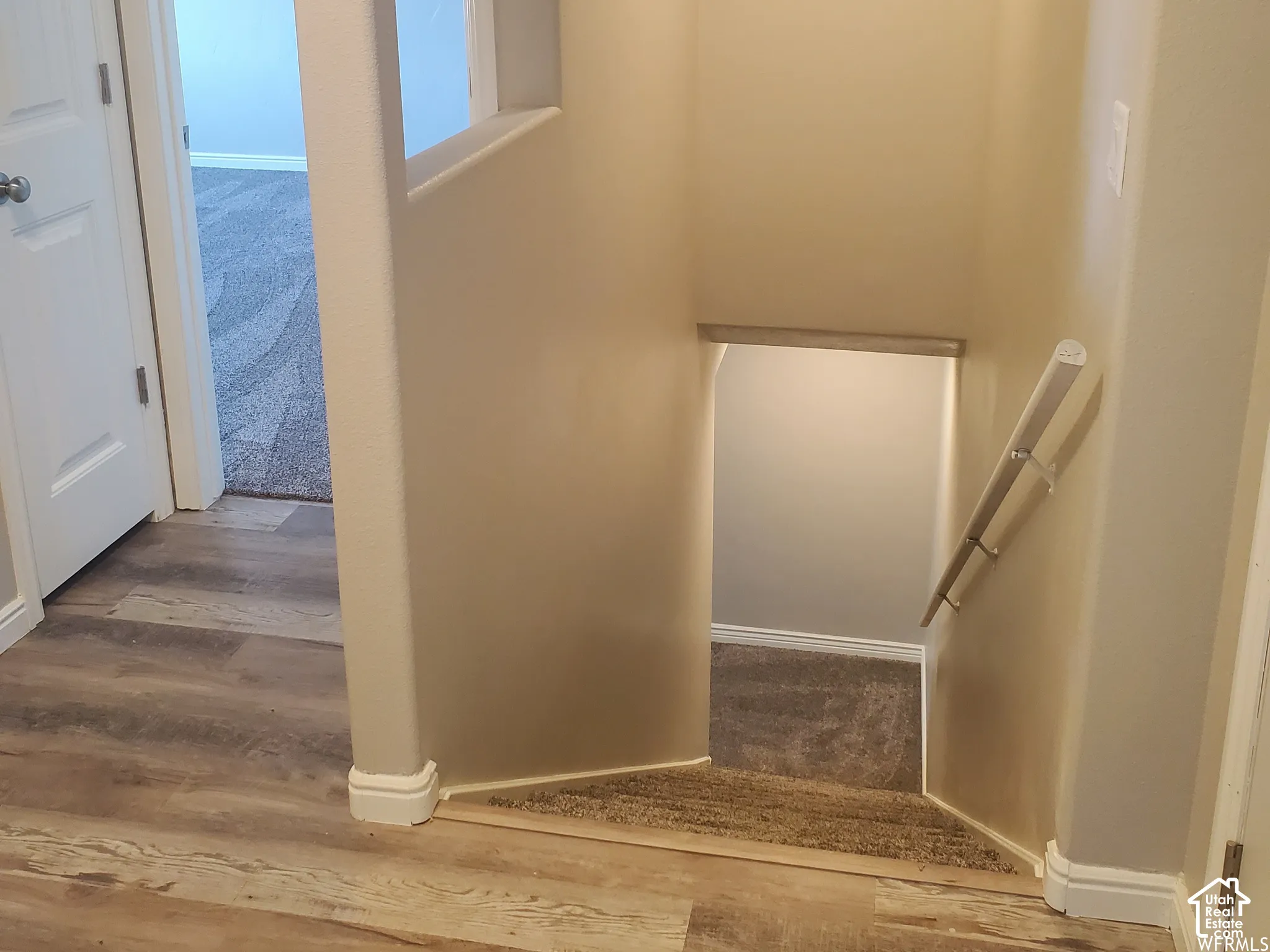 Staircase featuring carpeted steps, a wall-mounted metal handrail, wood-finish flooring, and a partial partition wall