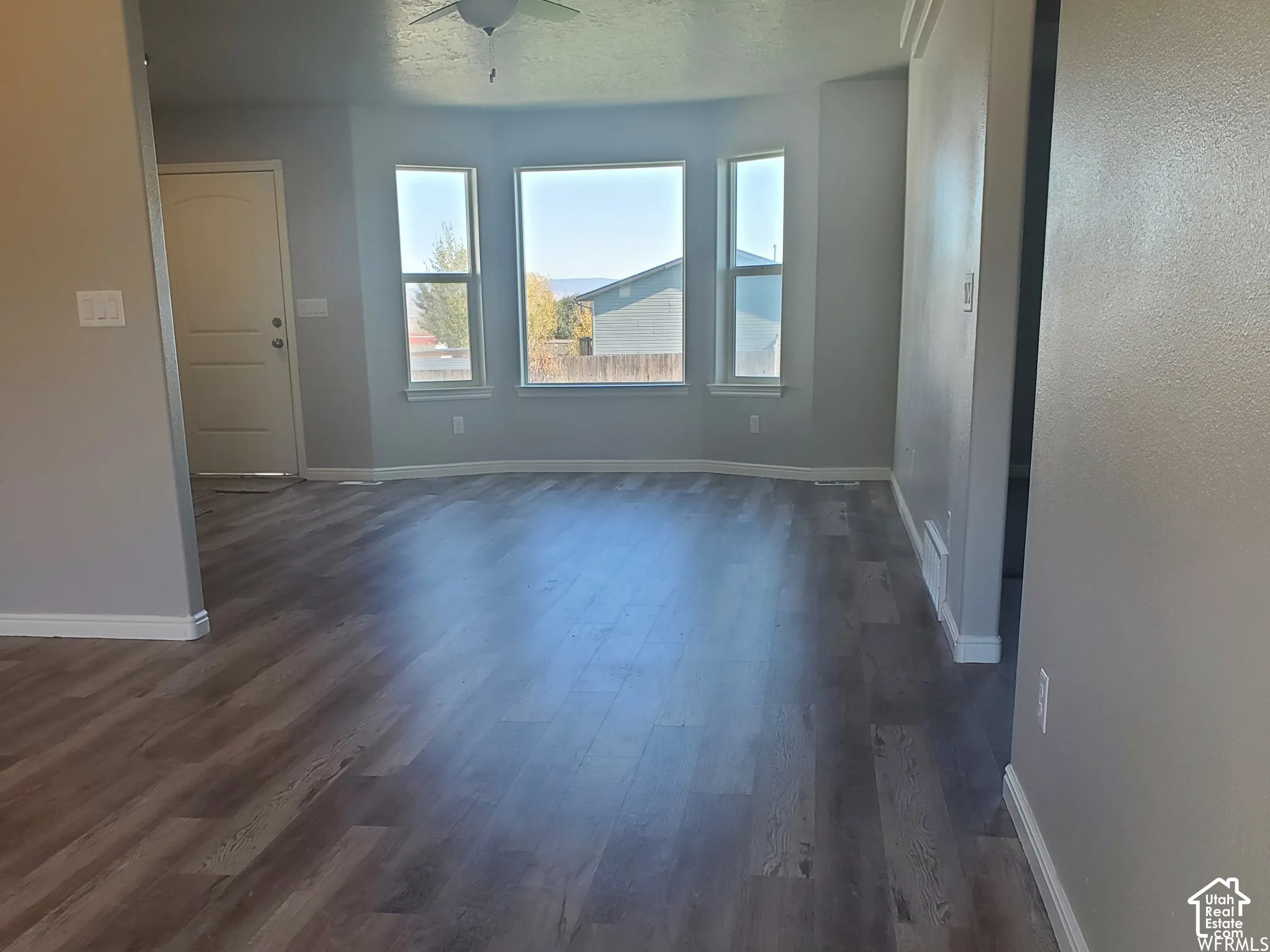 Open floor plan featuring wood-finish flooring, a bay window, and a ceiling fan