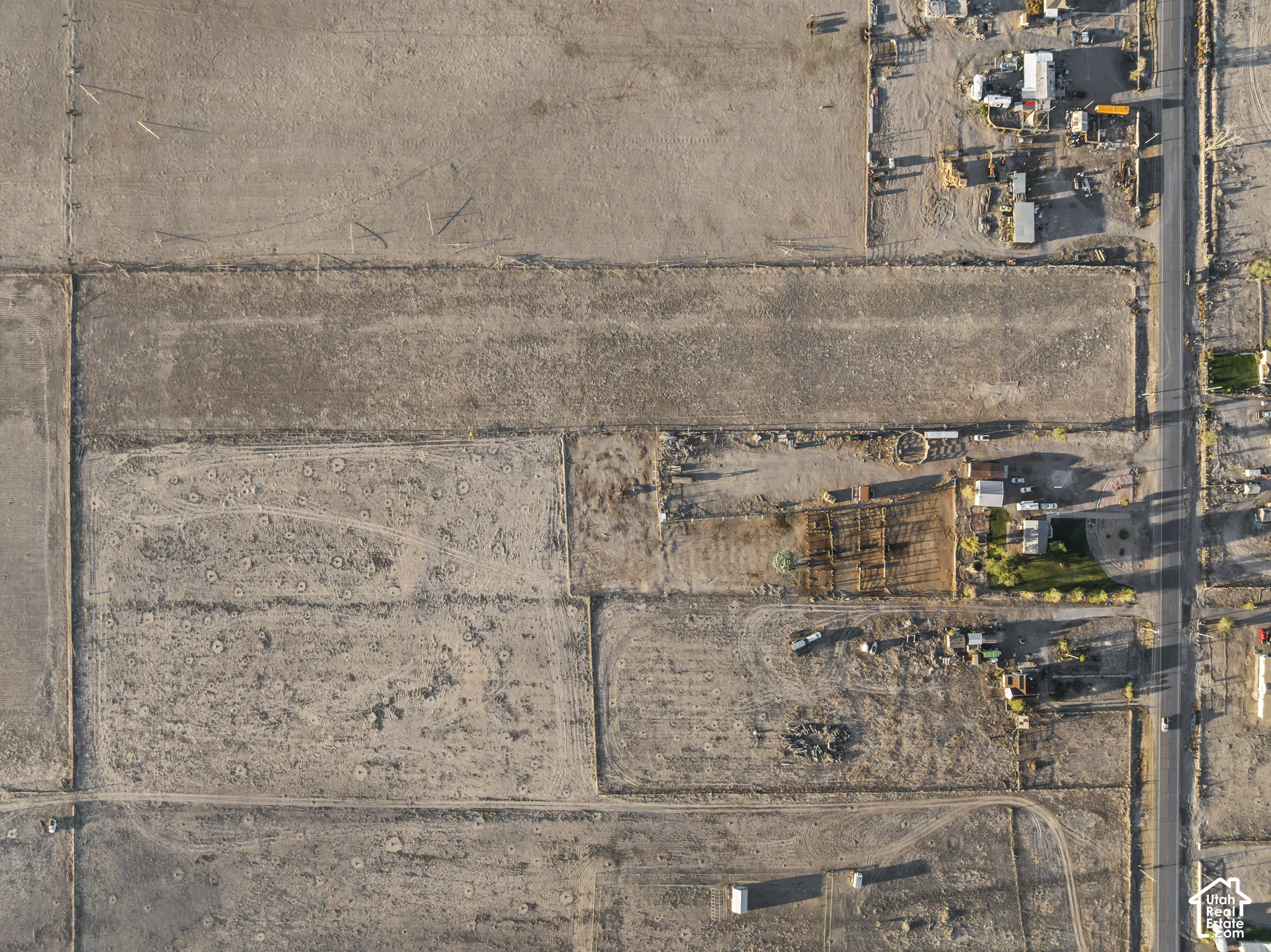 Aerial perspective of an expansive land parcel featuring open terrain, established perimeter fencing, and direct access to a paved thoroughfare