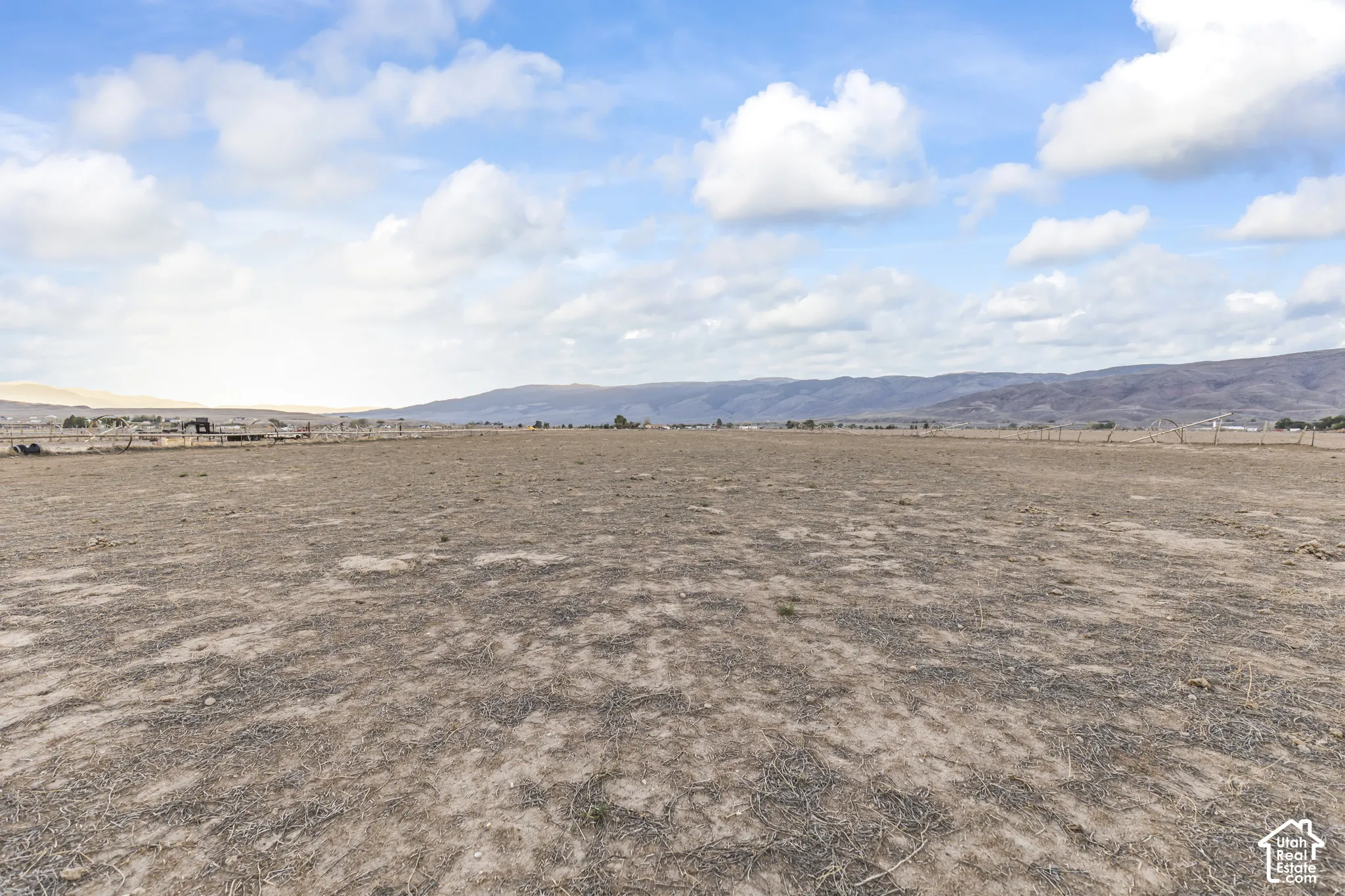Expansive open lot featuring native ground cover, perimeter wire fencing, and mountain topography