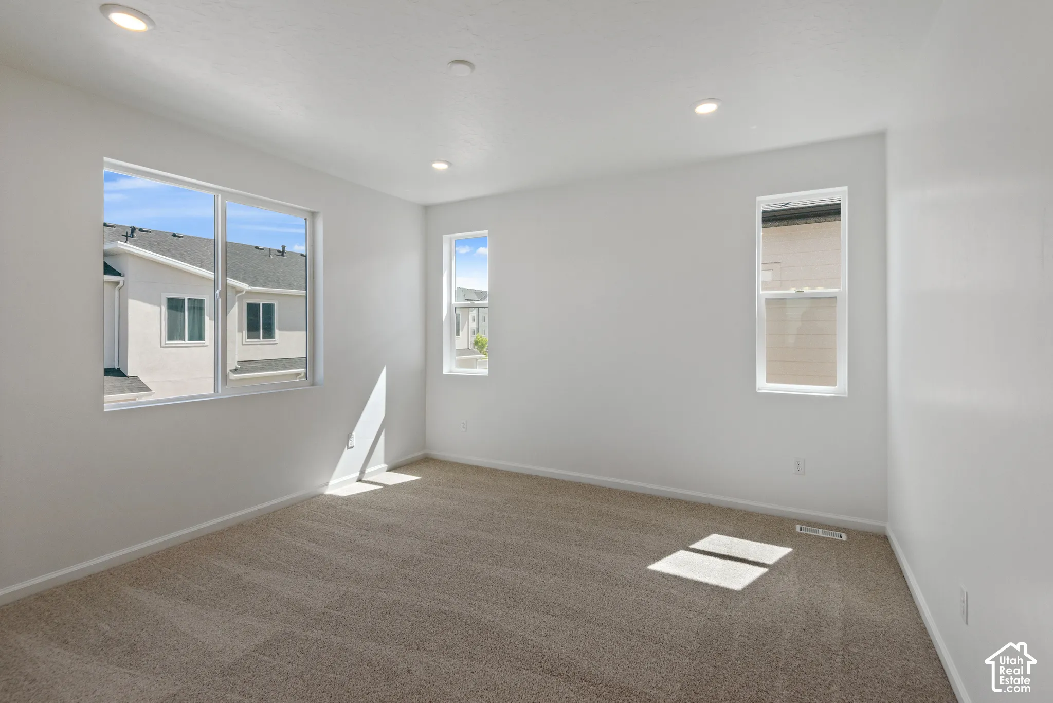 Neutral-toned wall-to-wall carpeting, recessed ceiling lighting, and multiple windows providing natural illumination