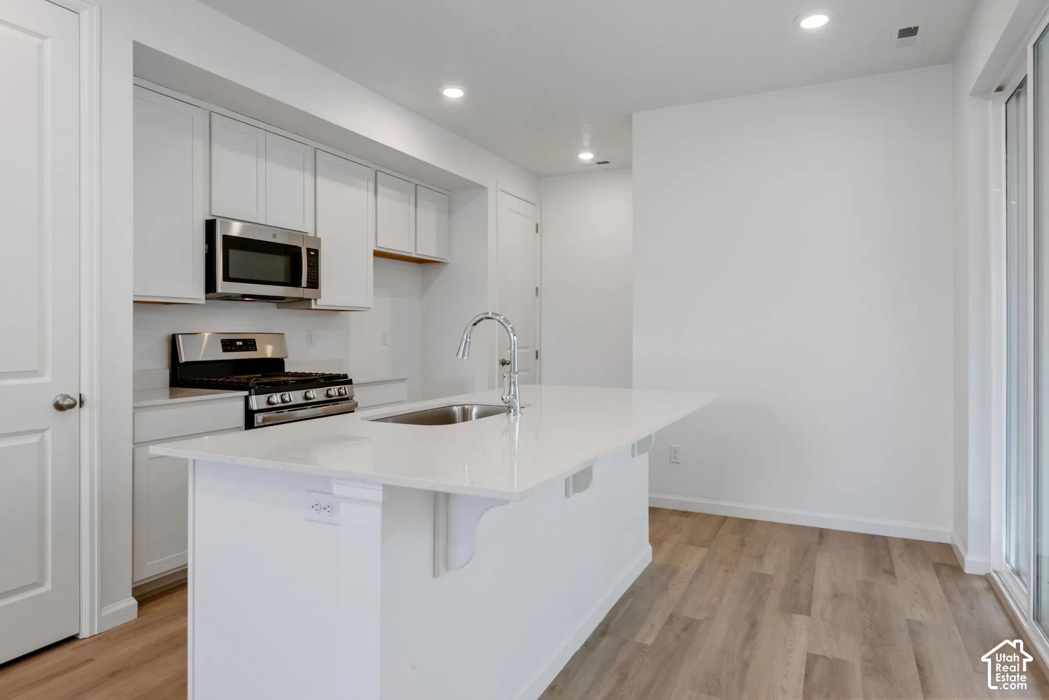 Kitchen featuring white shaker-style cabinetry, quartz countertops, a central island with a stainless steel sink, stainless steel appliances, and wood-finish flooring