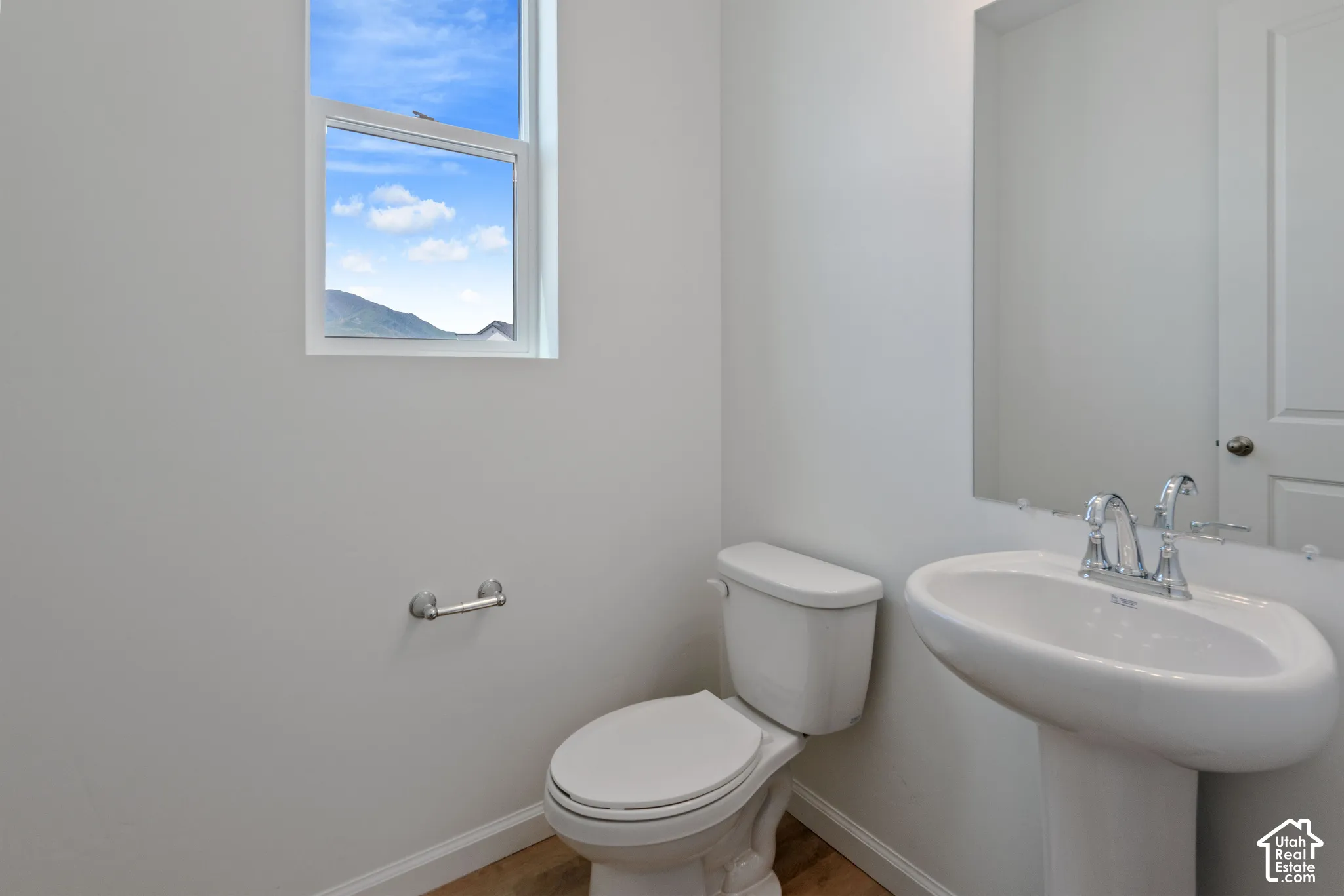 Powder room featuring a white pedestal sink, polished chrome faucet, large rectangular mirror, and wood-finish flooring