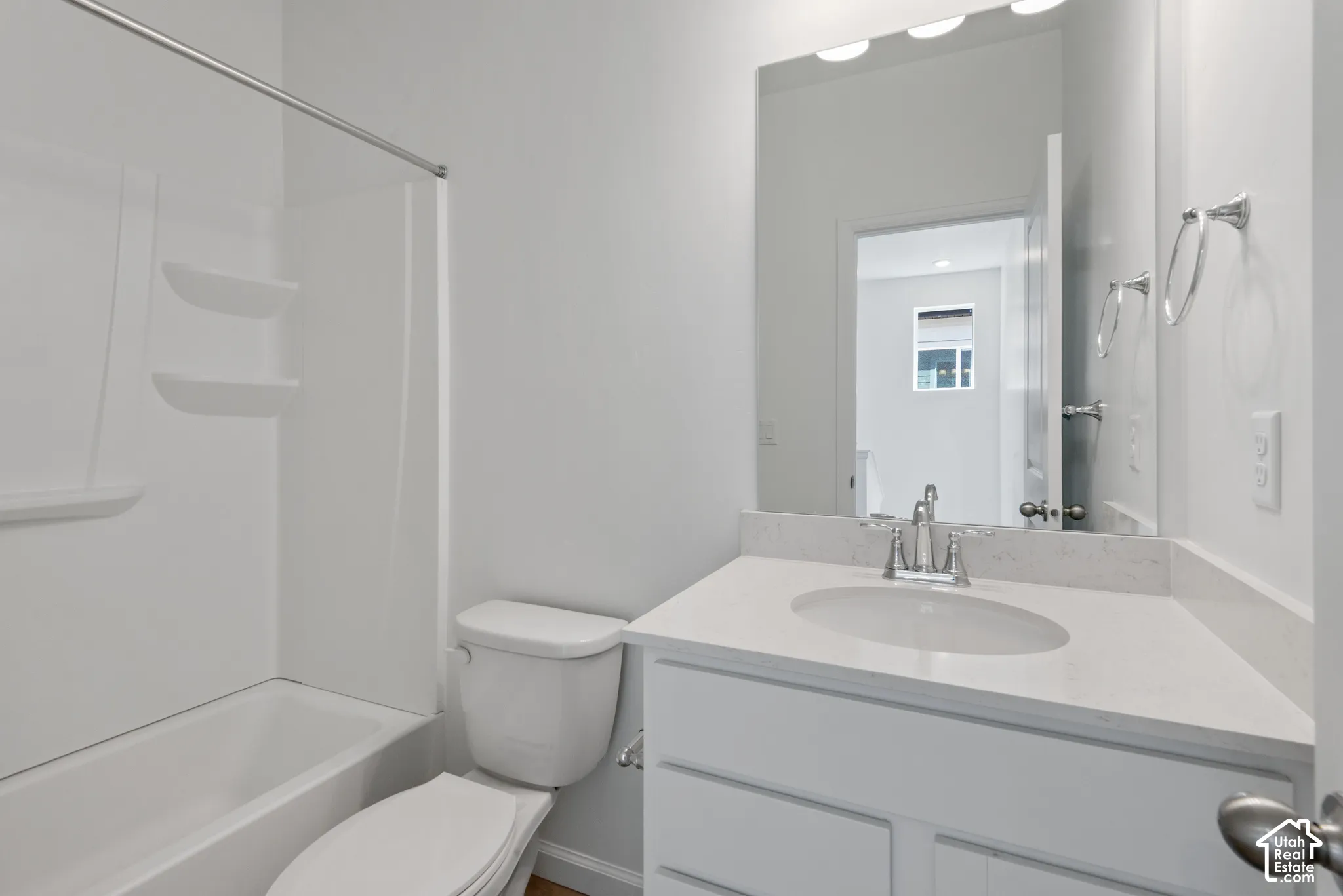 Bathroom featuring a vanity with a white countertop and oval under-mount sink, large wall-mounted mirror, brushed nickel faucet, and a tub-shower combination with built-in shelving