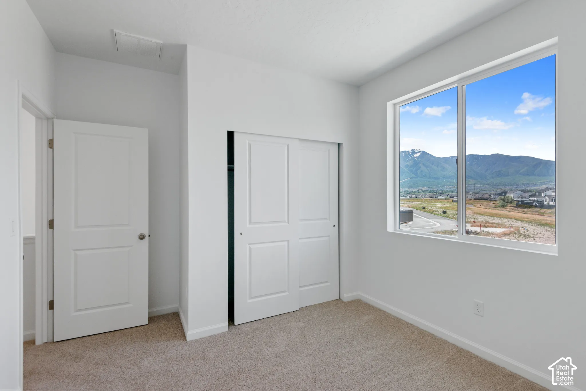 Room featuring neutral carpeting, a dual-panel closet, a swing-panel door, and a large window showcasing mountain scenery