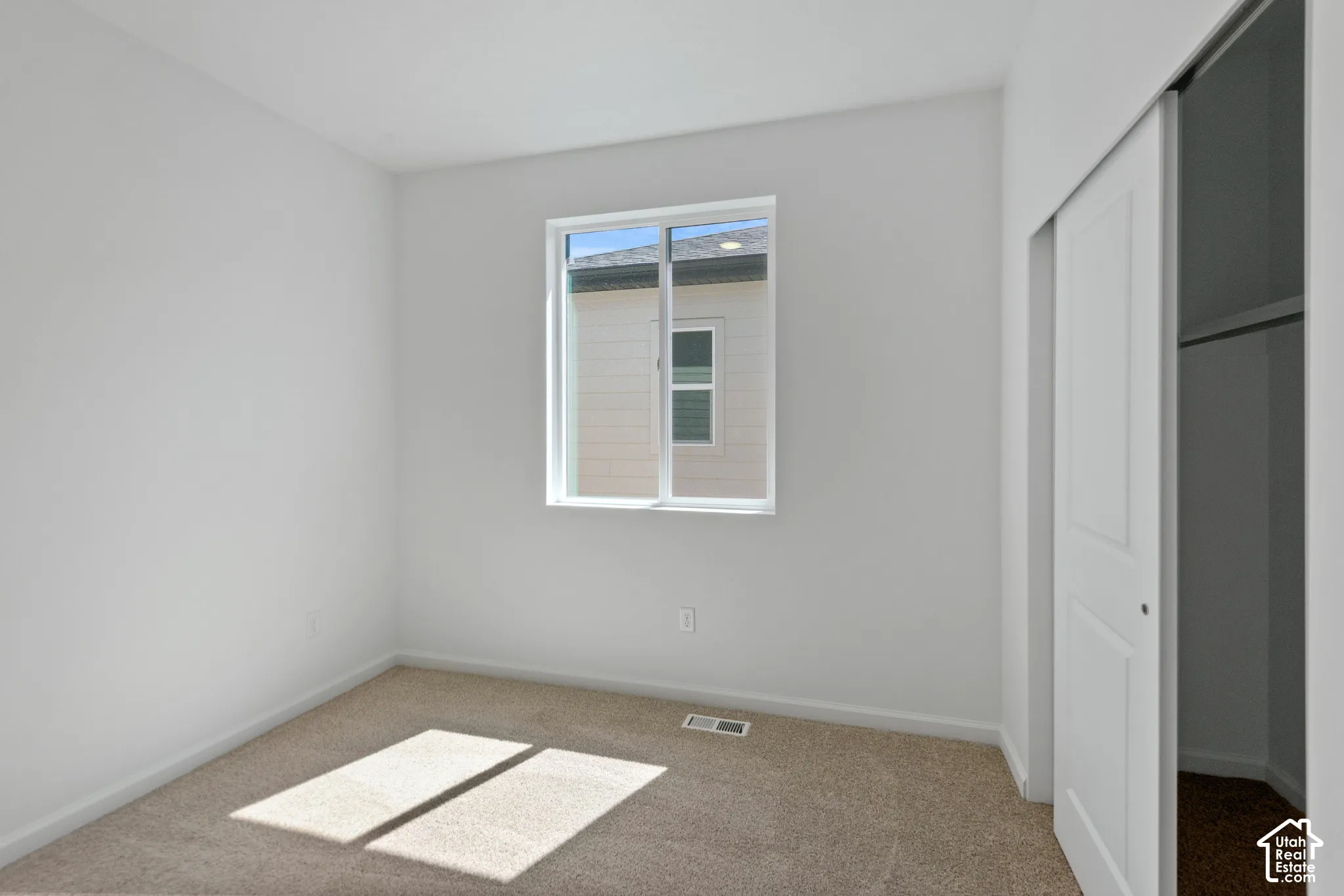 Neutral-toned interior room featuring wall-to-wall carpeting, a single-pane sliding window, and a closet with a sliding panel door