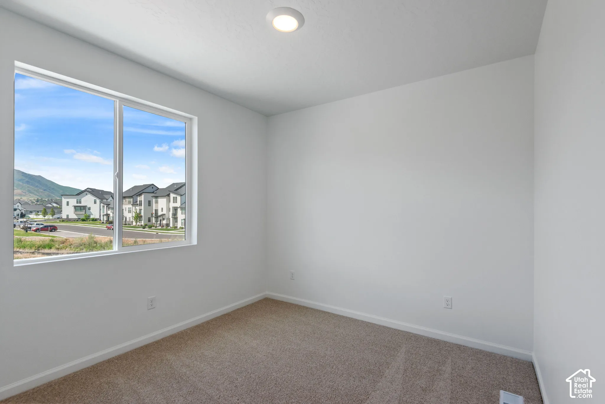 Interior space featuring neutral wall tones, wall-to-wall carpeting, a flush-mount ceiling light fixture, and a large window showcasing mountain scenery