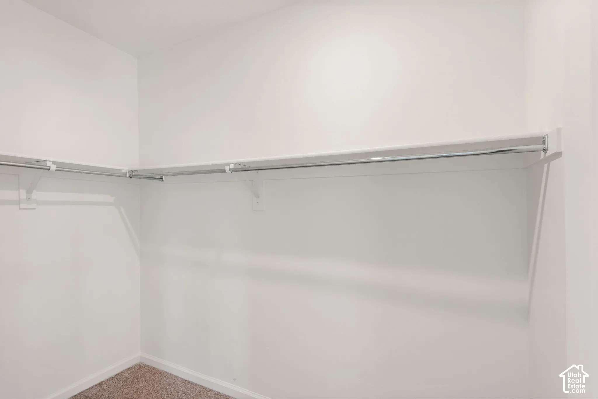 Walk-in closet featuring white walls, carpeting, and tiered metal shelving with integrated clothing rods