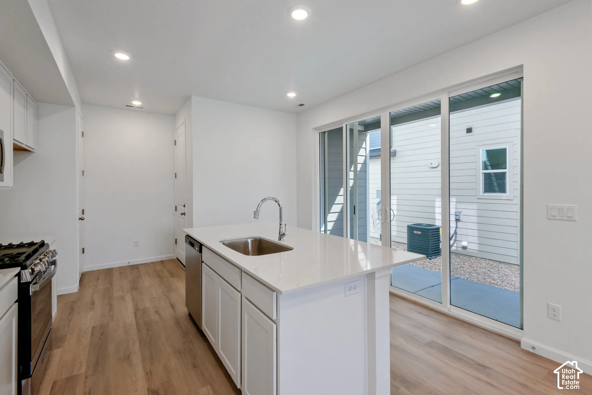 Kitchen featuring wood-finish flooring, white cabinetry, a center island with a stone-surface countertop, an integrated stainless-steel sink, and a large sliding glass door