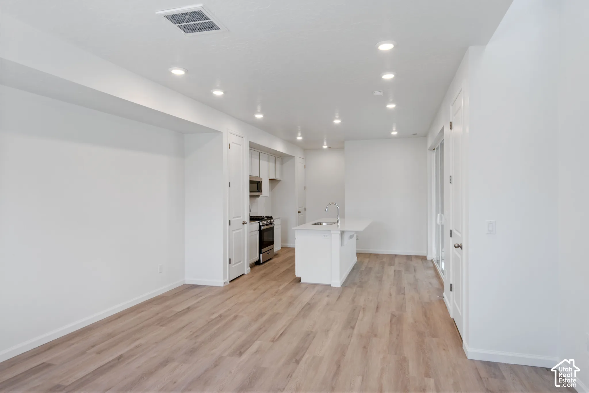 Kitchen featuring wood-finish flooring, recessed lighting, a central island with a sink, white cabinetry, and stainless steel appliances