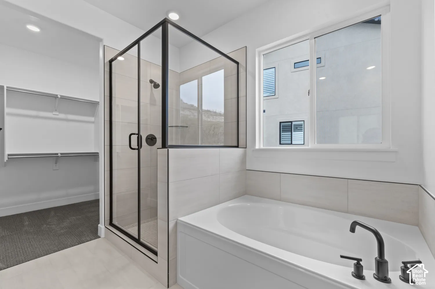 Glass-enclosed shower with matte black fixtures, deep soaking tub with wall-mounted matte black faucet, and large-format tile surround