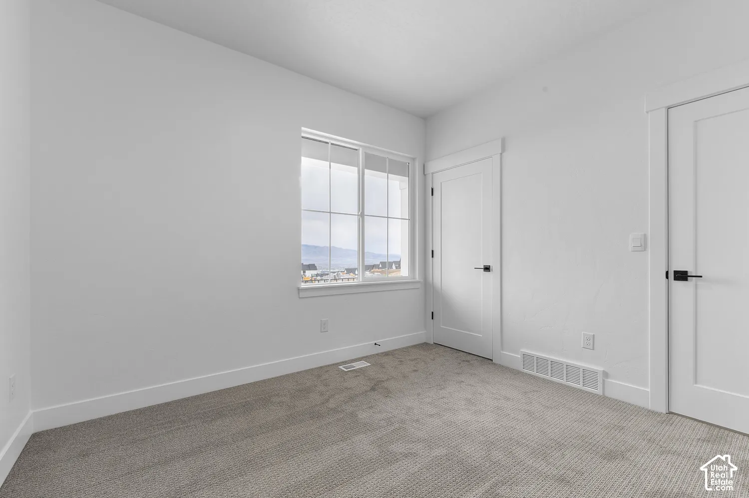 Neutral-toned carpeting, crisp white wall finish, white interior doors with matte black hardware, and grid-patterned window featuring exterior scenery