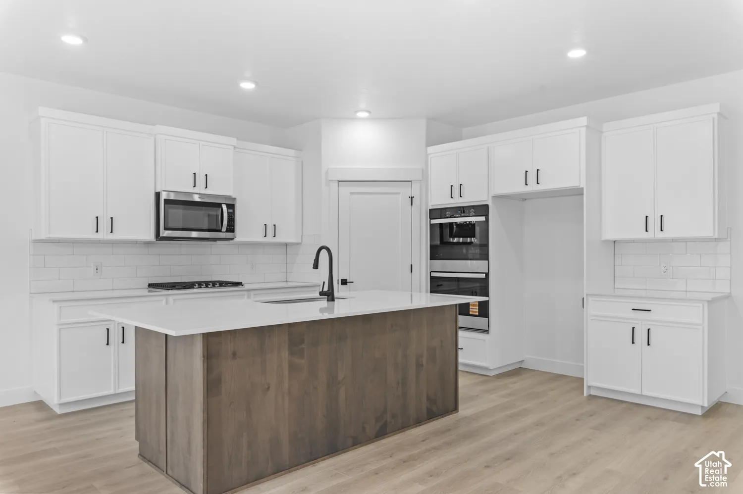 Kitchen featuring white cabinetry with matte black hardware, stone-surface countertops, wood-finish kitchen island, subway tile backsplash, and built-in double wall ovens