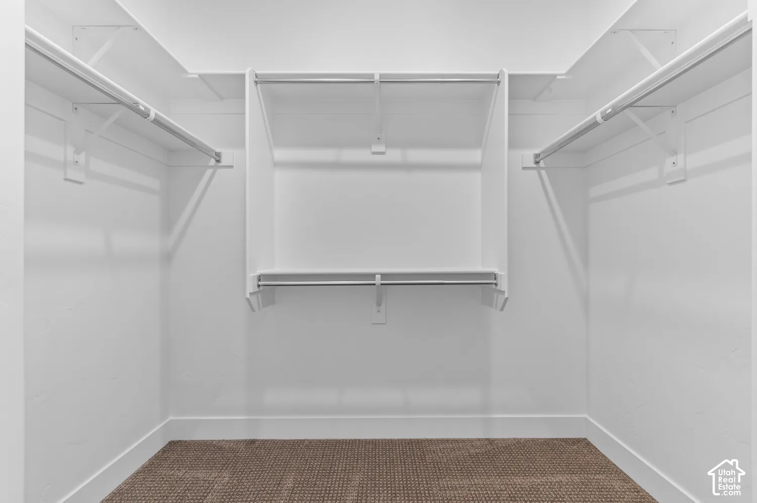 Walk-in closet featuring tiered white shelving, metal hanging rods, and neutral-toned carpeting