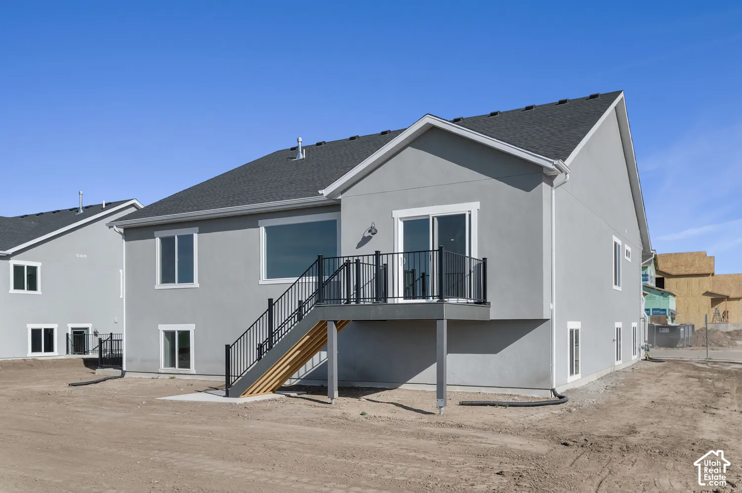 Two-story exterior featuring a gray stucco facade, asphalt shingle roofing, and elevated rear deck with metal railings and stairs