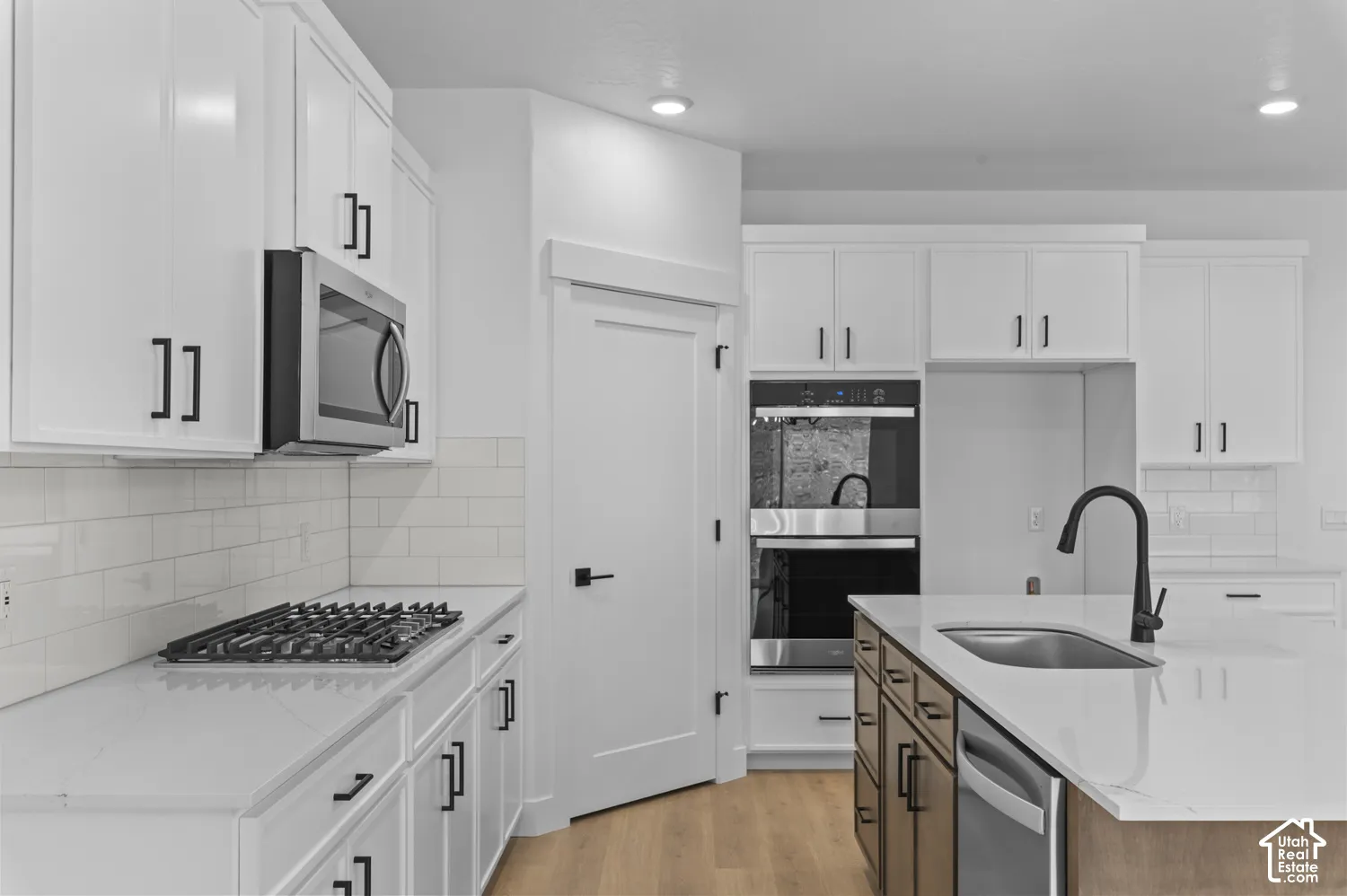 Kitchen featuring white shaker-style cabinetry, quartz countertops with a waterfall edge on the island, stainless steel double wall ovens, a gas cooktop, and matte black hardware