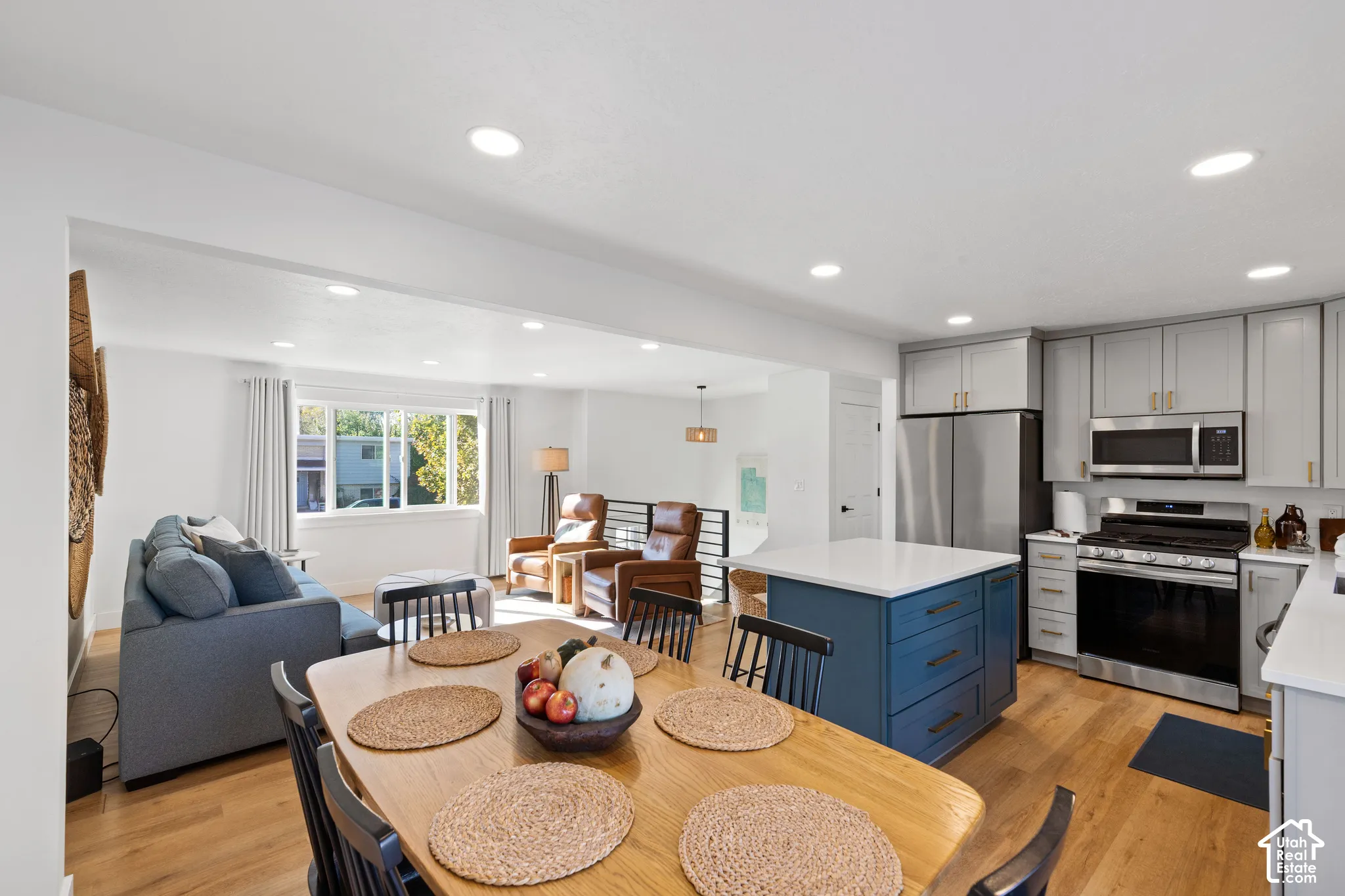 Kitchen featuring a contrasting blue island with quartz countertop, light-toned cabinetry, stainless steel appliances, and wood-finish flooring with recessed lighting throughout