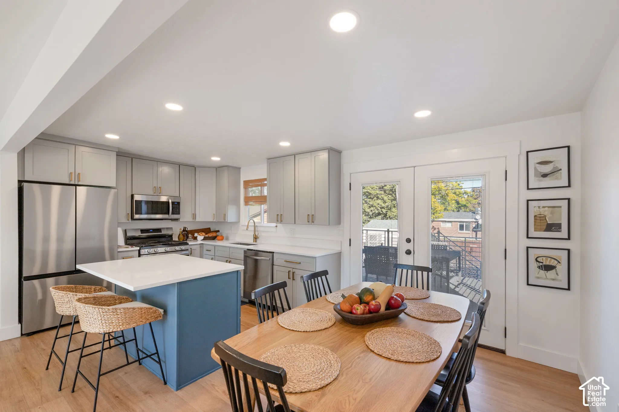 Kitchen featuring grey shaker-style cabinetry, white solid-surface countertops, a contrasting blue island, stainless steel appliances, and wood-finish flooring