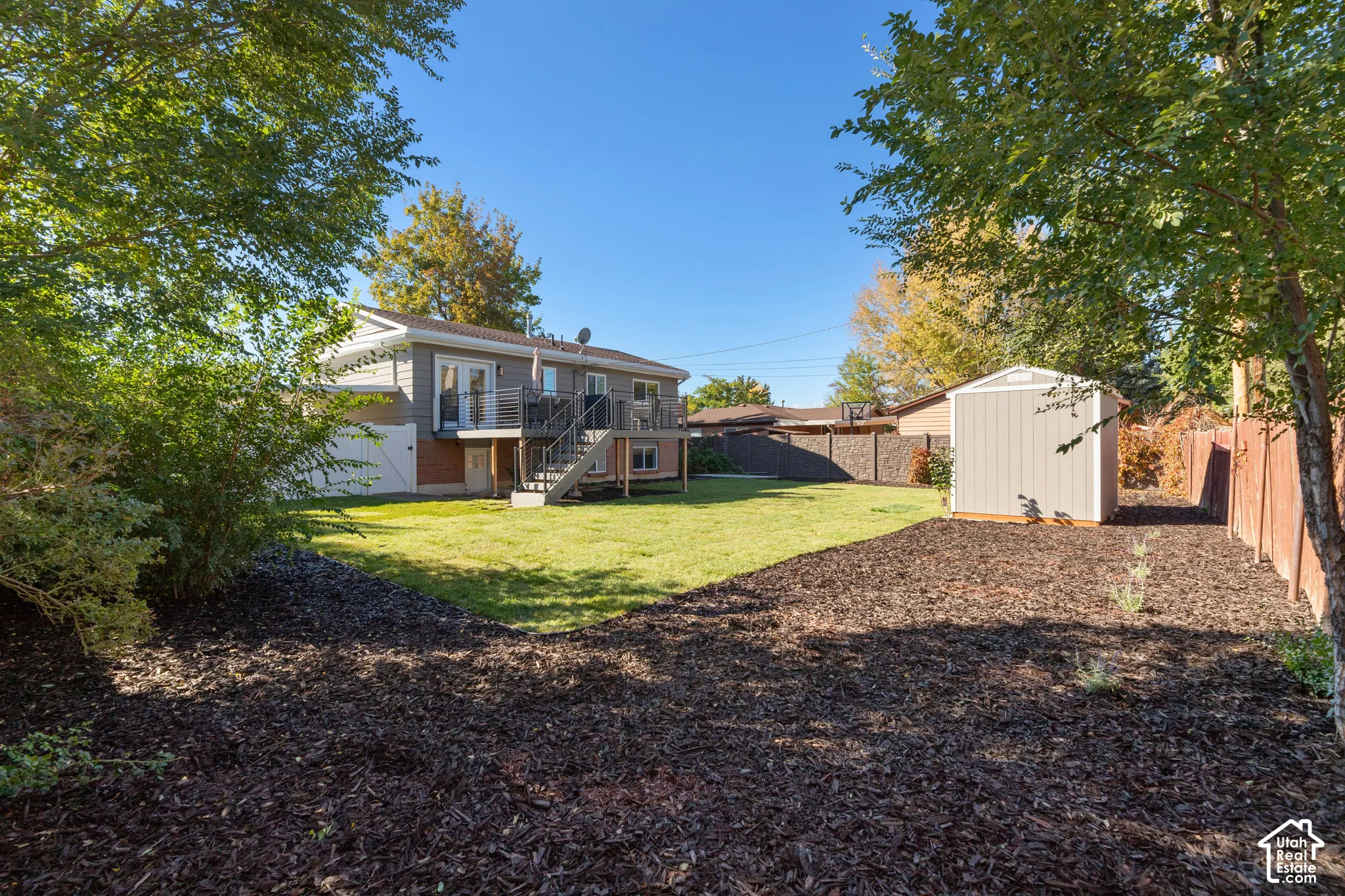 Expansive backyard featuring a manicured lawn, a detached storage structure, multi-level wood-finish deck with metal railings, and a perimeter fence