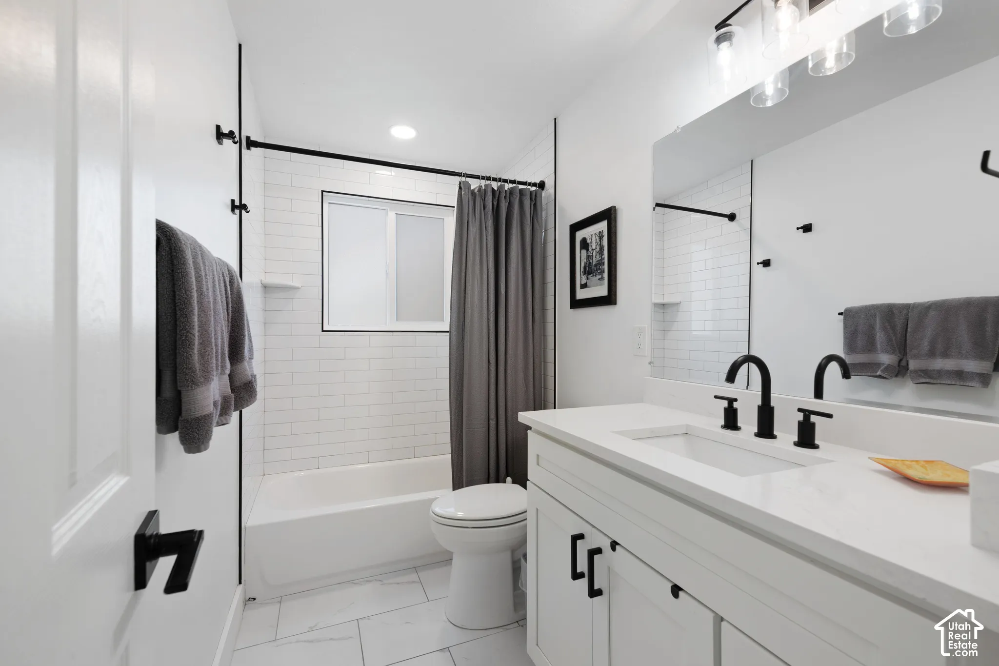 Bathroom featuring a white vanity with a solid-surface countertop, matte black widespread faucet, subway-tiled tub surround, and tile flooring