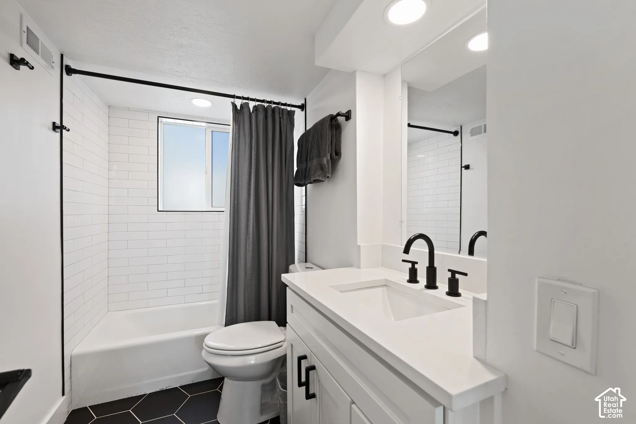 Bathroom featuring a white vanity with a quartz countertop, matte black faucet hardware, white subway tile shower surround, and black hexagonal floor tiling